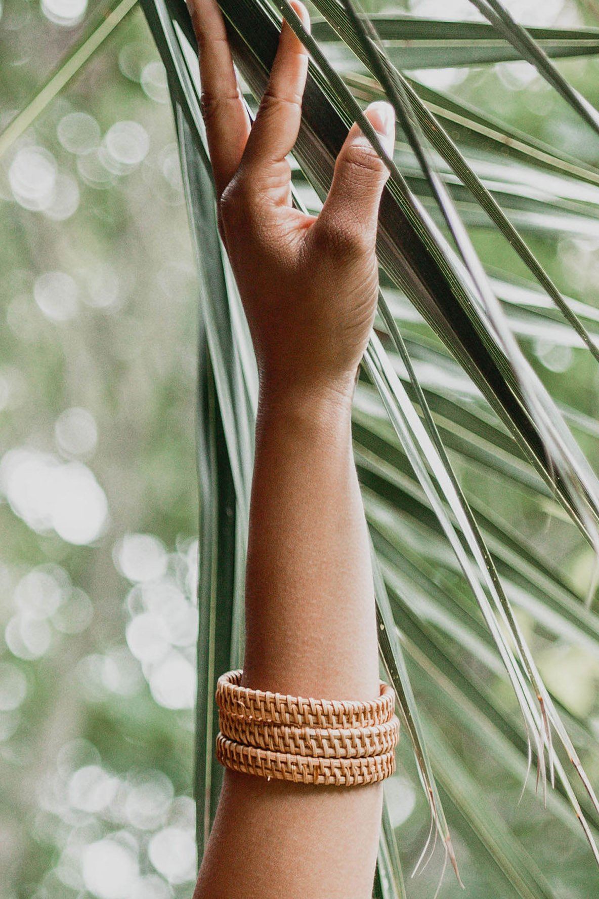 Hand with a bracelet touching palm leaves with a blurred green background