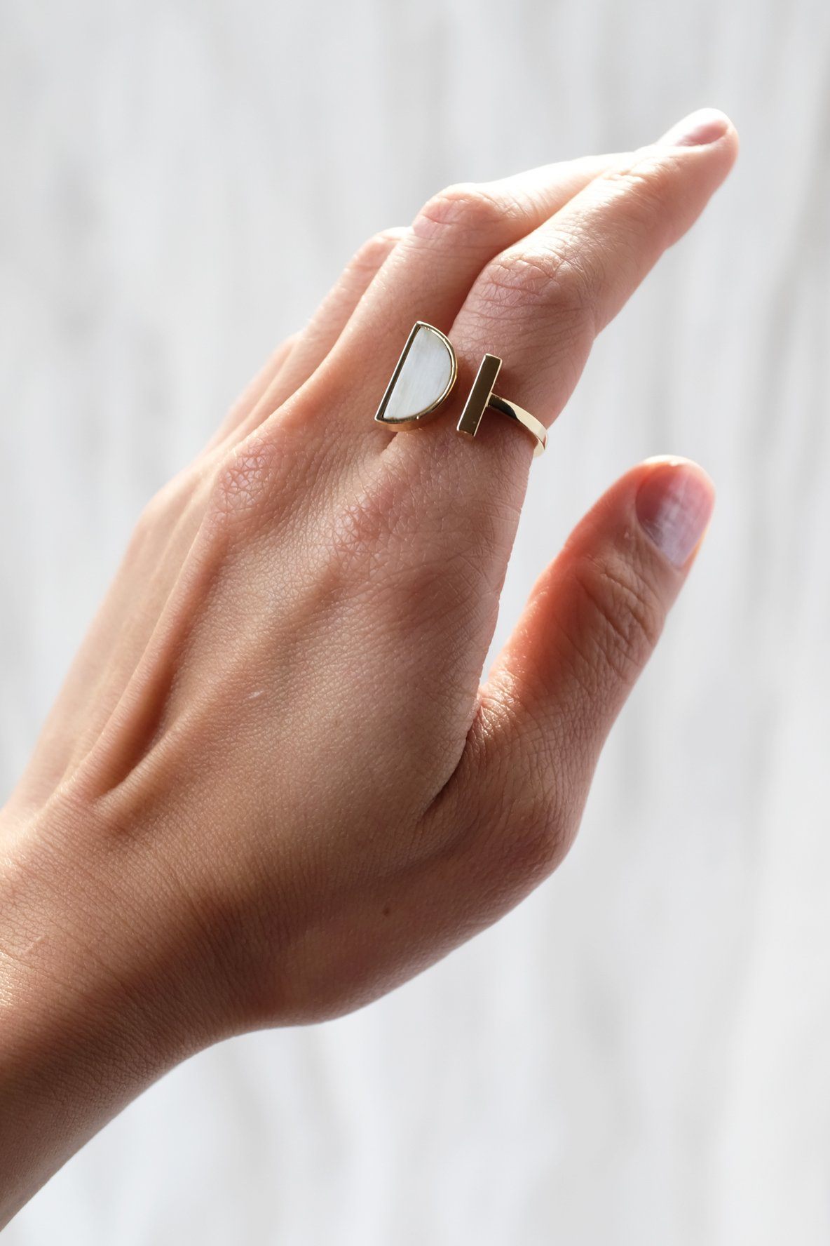 Hand wearing a ring with a white stone on a plain background